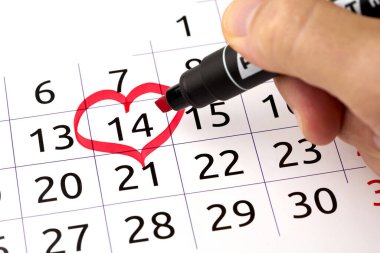 Kırmızı kalemli el takvimde kalp şekilli sevgililer gününü vurgular