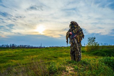 Kamuflaj üniformalı havalı oyuncu sahada elinde bir tüfek tutuyor.