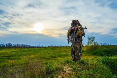 Kamuflaj üniformalı havalı oyuncu sahada elinde bir tüfek tutuyor.