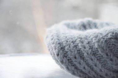 Gri örülmüş yünlü bir eşarp, düzgünce katlanmış, arka planda bulanıklık var. Sıcak kış arkaplanı, açık renkli sıcak. Metne yer var..