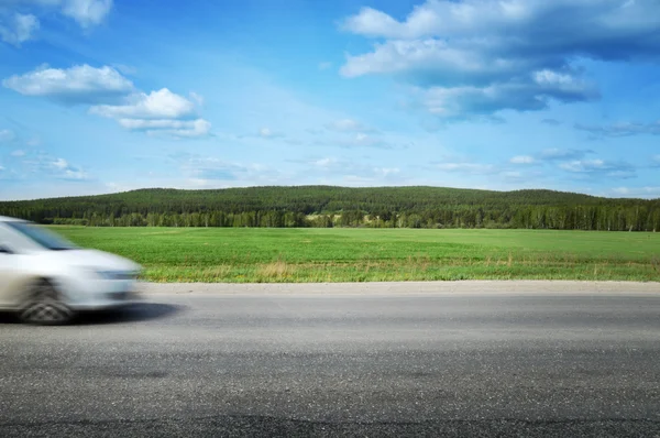 Das Auto rast über eine Landstraße, umgeben von Wald und blauem Himmel lizenzfreie Stockbilder