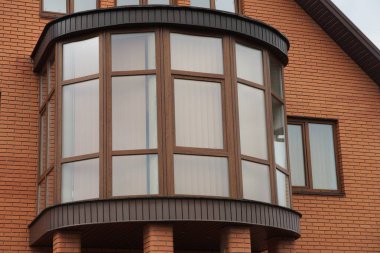 Pencereleri olan özel bir evin kahverengi duvarında büyük kapalı camlı bir balkon.