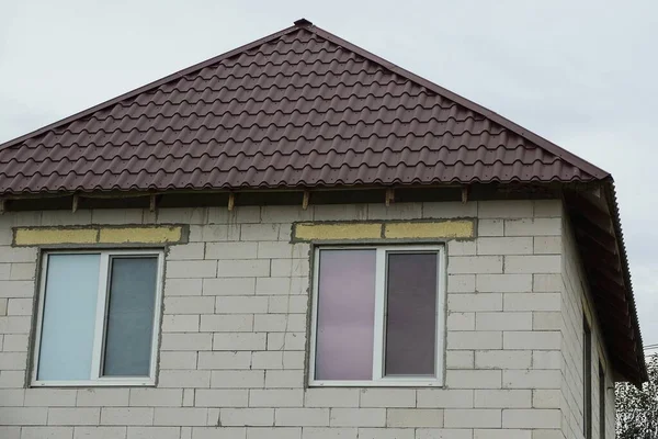 空に向かって通りの茶色の瓦屋根の下に2つの窓がある民家の灰色のレンガ屋根裏部屋 — ストック写真