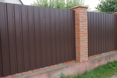  Kırsal bir sokakta yeşil çimlerde metal ve kahverengi tuğlalardan oluşan bir duvar.