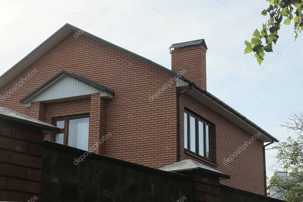 large brown brick house with windows behind a fence against a blue sky