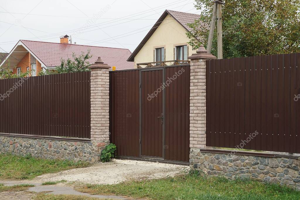  brown metal gate and part of the wall of the fence made of wooden boards and bricks on the street