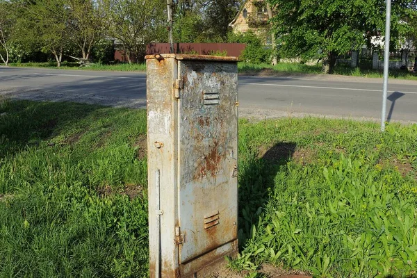 one old closed metal box for electrical wires in brown rust outside in green grass