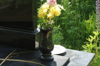 one black marble vase with colored artificial flowers stands at the monument on the grave  clipart