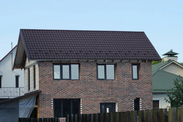 big brown brick house with windows behind a fence against a blue sky