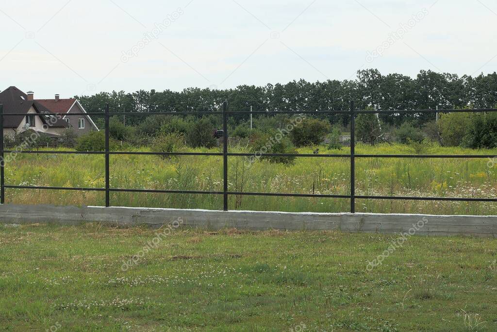 black iron frame of an unfinished fence on a gray concrete foundation outside in green grass