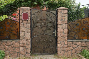 Siyah dövmeli, kahverengi metal kapılı bir kapı ve caddede taş bir çitin parçası.