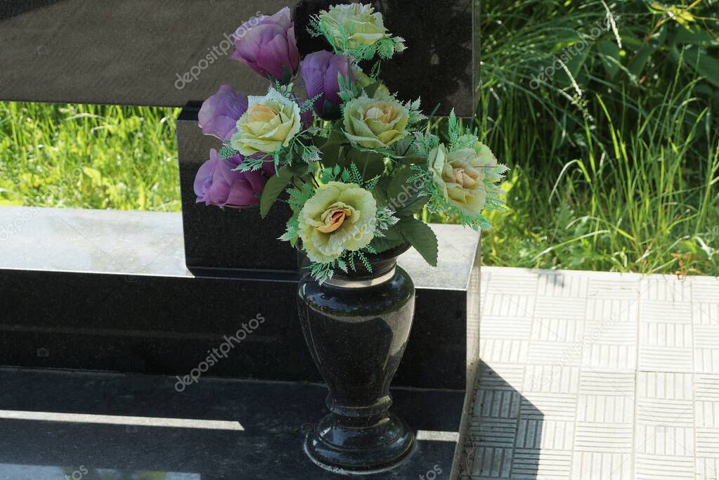  black marble vase with colored artificial flowers stands at the monument on the grave