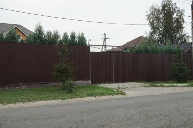  Kapalı kahverengi metal kapı ve yeşil çimenlikteki uzun çitin bir kısmı