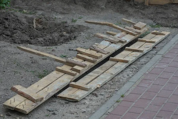 Long brown wooden formwork boards lie on gray ground by the sidewalk in the street — Stock Image Long Brown Wooden Formwork Boards Lie Gray Ground Sidewalk Street Stock Image
