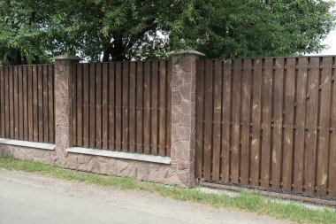 Yeşil bitki örtüsünde, tahta tahtalardan ve taşlardan yapılmış bir çitin kahverengi duvarının bir parçası.