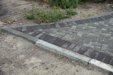 Yere yakın gri kaldırım levhaları ve sokakta yeşil çimenler.