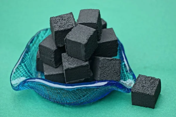 a pile of black square charcoal for a hookah in a blue glass ashtray stands on a green table