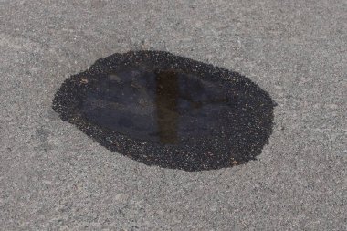 Gri, kuru asfalt yolda bir su birikintisinde siyah su.