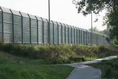 Sokakta yeşil çimlerde, mavi gökyüzüne karşı uzun, gri, demir bir çit.