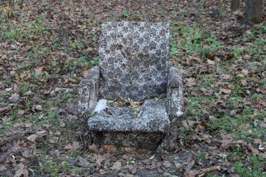 Bir sonbahar parkında yeşil çimlerin ve kahverengi yaprakların üzerinde duran eski gri bir sandalye.