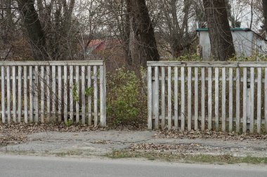 Gri bir yolun kenarındaki beyaz tahtalardan yapılmış eski ahşap çit