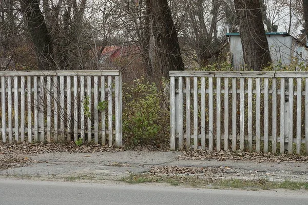 Gri bir yolun kenarındaki beyaz tahtalardan yapılmış eski ahşap çit