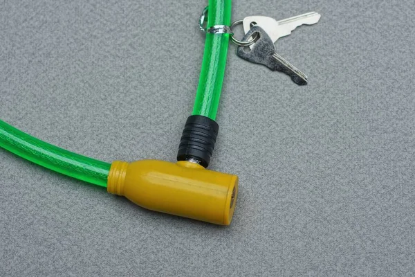 自行车锁的一部分 装有黄色金属芯和绿色塑料电缆 两把钥匙放在灰色的桌子上 — 图库照片
