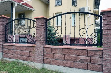 Çitin duvarının bir kısmı kahverengi tuğlalardan ve sokaktaki siyah demir keskin çubuklardan yapılmış.