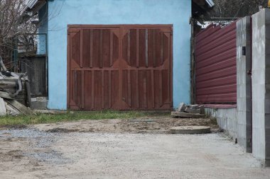 Kırsal bir sokakta mavi beton duvarı ve kahverengi metal kapıları olan özel bir garajın ön cephesi.