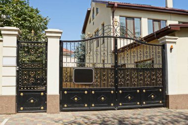 Büyük siyah metal kapılar ve demir desenli kapalı bir kapı ve kaldırımın dışındaki beton çitin bir parçası.