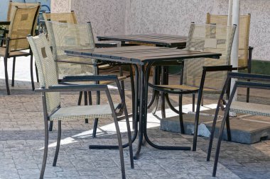 gri siyah sandalyeler ve dışarıda kaldırımda bir masa standı. Bir yaz restoranının beton duvarının yanında.