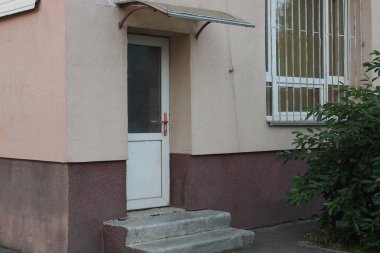 Beton kahverengi duvarda camla kaplı beyaz kapalı bir kapı ve dışarıda gri basamaklar.