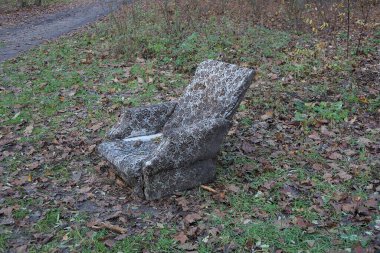 Bir sonbahar parkında atılmış eski bir gri sandalye yeşil çimlerde ve kahverengi yapraklar arasında duruyor.