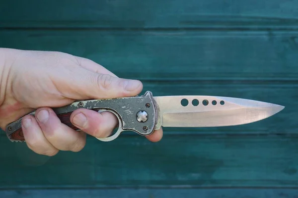 hand holds a gray steel hunting knife on a green background
