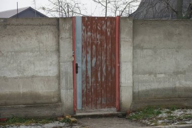 Kırsal bir sokakta kapalı bir kahverengi kapı ve gri beton çit.