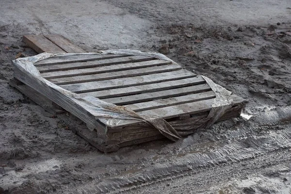 one old wooden pallet lies in gray mud and wet ground on the street on the road