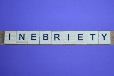 Gri kelime sarhoşluğu küçük kare tahta harflerle, eflatun arkaplanda siyah yazı tipiyle.