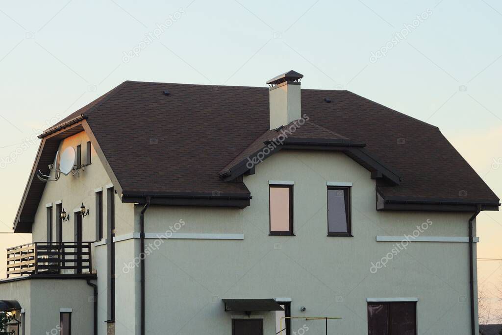 facade of a private house with gray wall windows and an open balcony under a brown tiled roof on the street against a blue sky