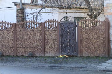 Kahverengi metal kapılı bir kapı, sahte desenli ve caddede taş bir çit var.