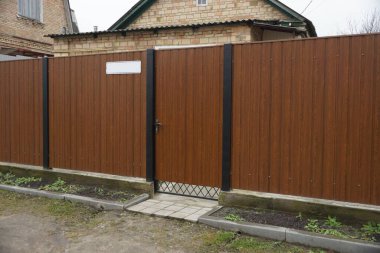 Kahverengi kapalı kapı ve caddede metal bir çit var.