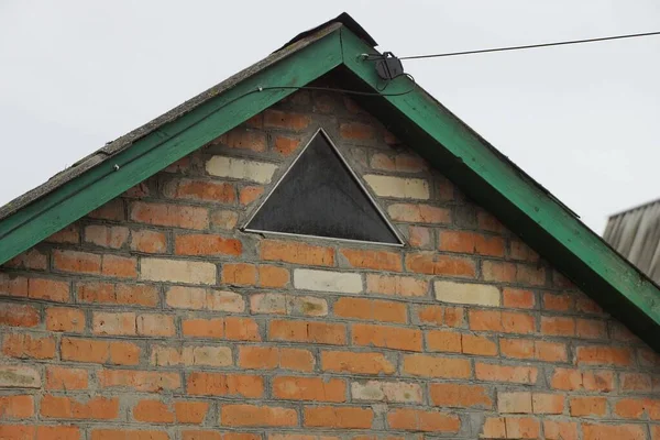 灰色の空に向かって通りに三角形の窓がある田舎の家の古い茶色のレンガ造りのロフト — ストック写真
