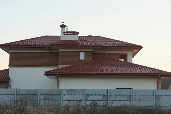 赤い瓦屋根の下の茶色い民家のファサード空に対して乾燥した草の中の灰色のコンクリートフェンスの後ろに — ストック写真