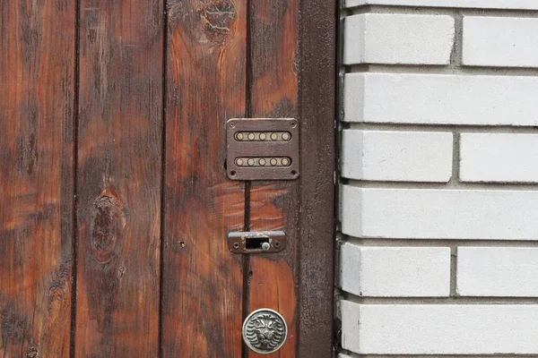 combination lock and doorknob on brown boards of a closed door against a white brick wall in the street