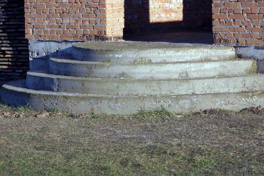 gri beton yarı dairesel eşik, yerde basamaklar ve dışarıda kahverengi tuğla bir duvara karşı yeşil çimenler.