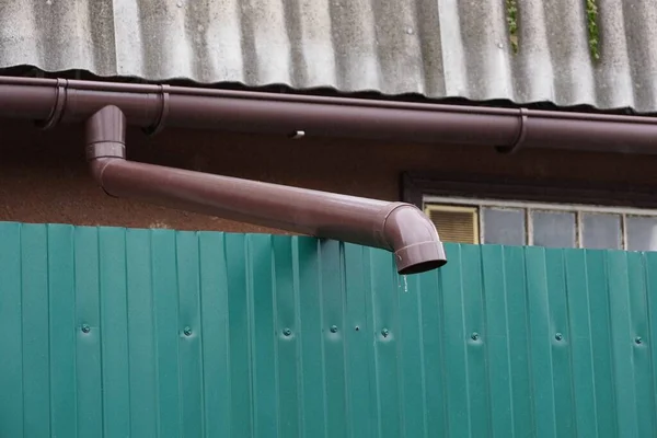 One Long Brown Plastic Gutter Pipe Green Metal Fence Wall — Stock Photo, Image