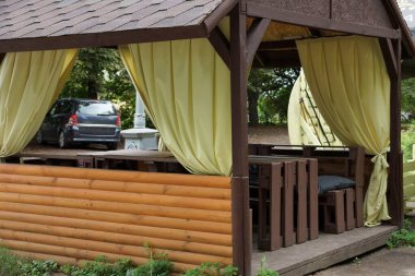 Kahverengi ahşap bir koruluğun parçası. Sokakta sarı perdeler var.