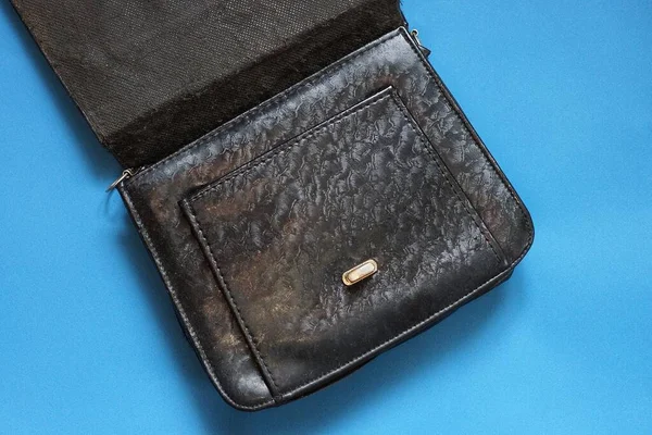 one black open leather bag lies on a blue table