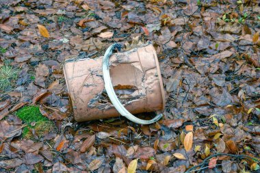 Eski kahverengi kırık ve erimiş plastik bir kova. Doğada düşen yaprakların üzerinde bir delik var.