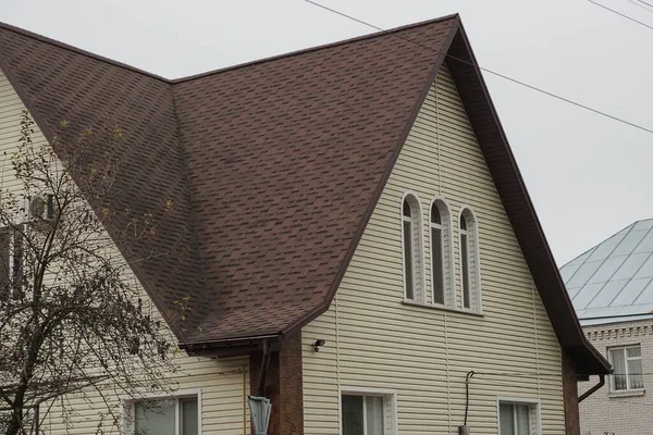 灰色の空に対して茶色のタイル張りの屋根の下に窓のある民家の一部 — ストック写真