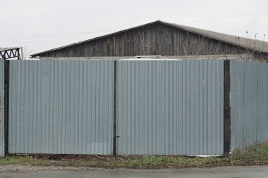 Büyük, gri bir demir kapı ve sokaktaki çitin bir kısmı.